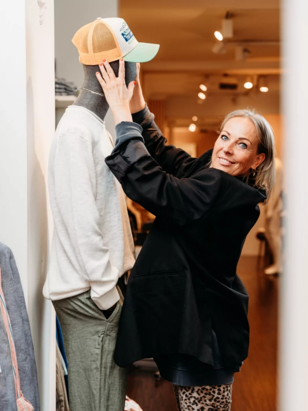 Eine lächelnde Frau in einem eleganten Business-Outfit blickt selbstbewusst in die Kamera. Der schlichte Hintergrund unterstreicht ihre Professionalität und Modebewusstsein.