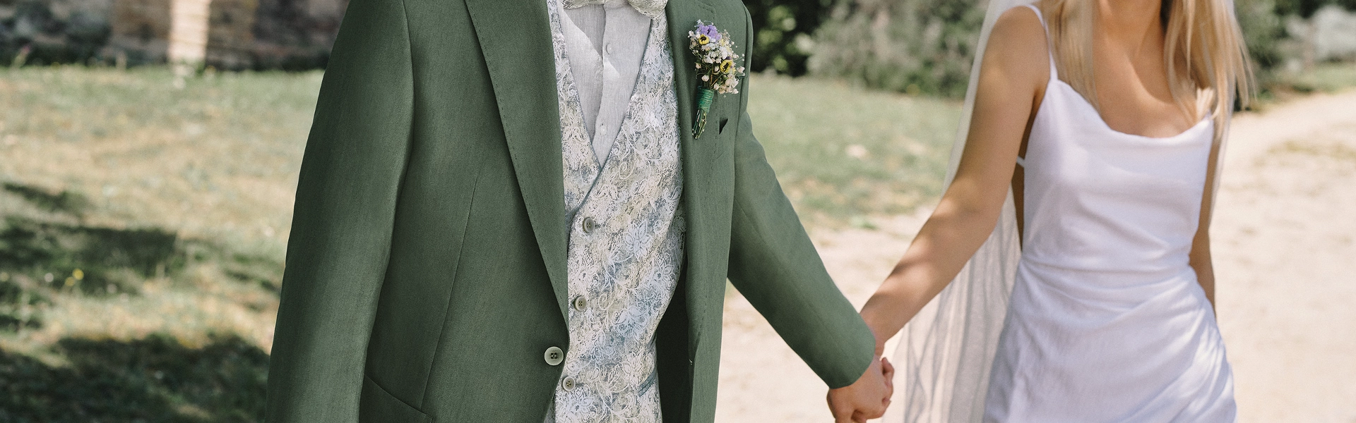 Bräutigam in grünem Hochzeitsanzug mit floraler Weste und Braut in weißem Kleid – stilvolle Hochzeitsinspiration vom Herrenzimmer Potsdam für individuelle Hochzeitsmode und persönliche Stilberatung.