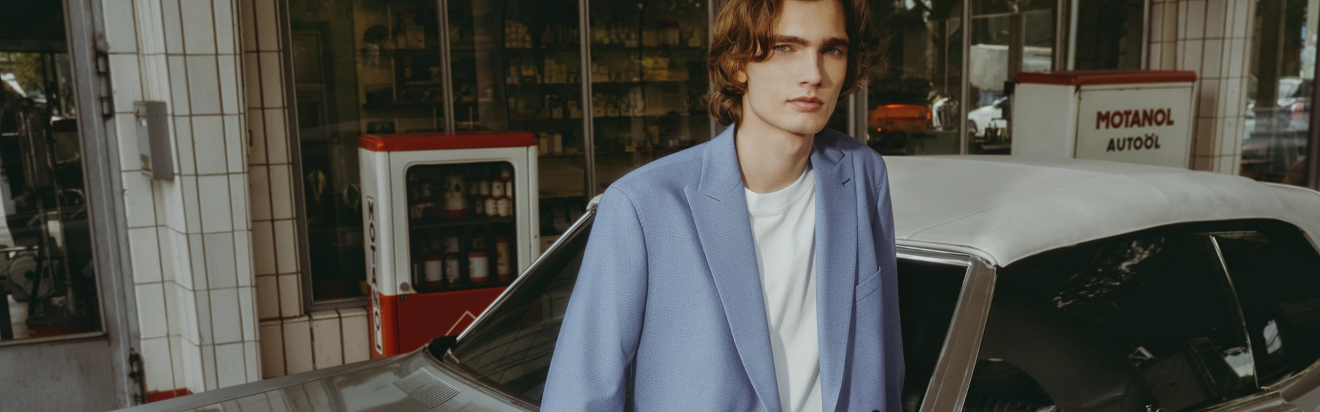 Junger Mann in modernem blauen Anzug vor Vintage-Tankstelle – modischer Look für Jugendweihe oder Konfirmation vom Herrenzimmer Potsdam mit urbanem Retro-Charme.