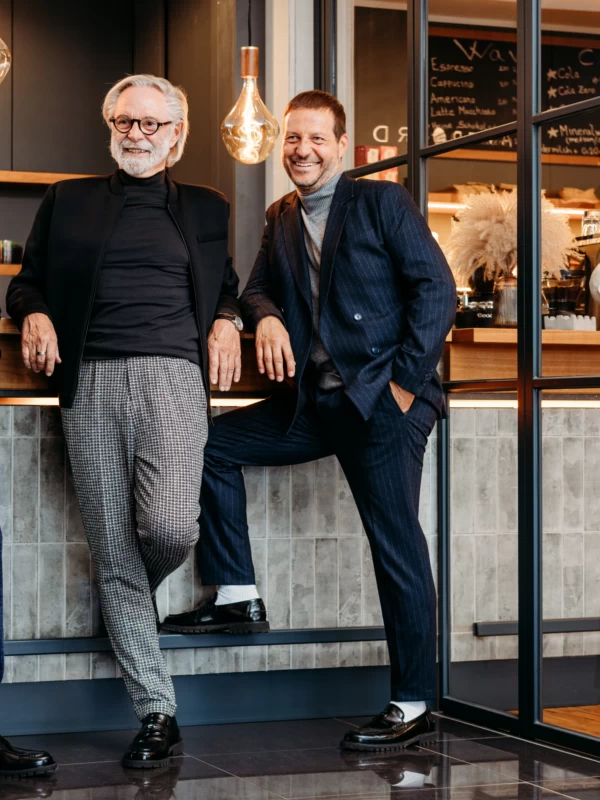 Mitarbeiter und Geschäftsführer des Herrenzimmer Potsdam in Anzügen lachend vor einer Bar im Café im Business-Look